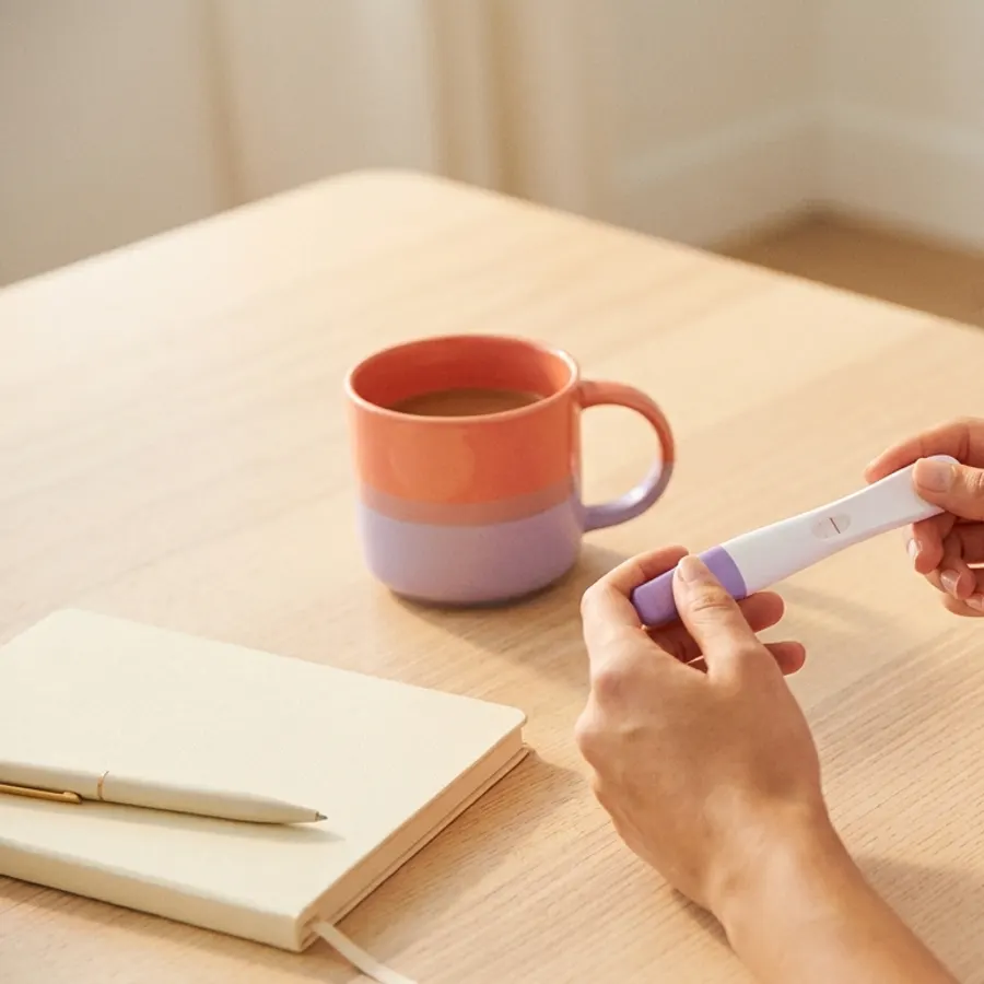 Les mains d’une femme tenant un test de grossesse sur une table claire